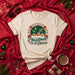 Christmas en el Barrio Tropical Holiday T-Shirt - Latino Christmas Tee with Palm Trees, Houses, Sugar Skulls, and Poinsettias - Unisex Soft Style Seasonal Apparel Mexicada